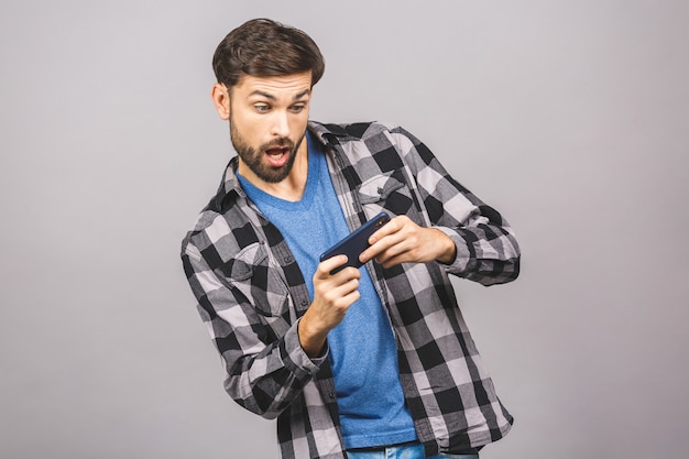 Portrait of an excited young man in casual playing games on mobile phone isolated over grey wall.