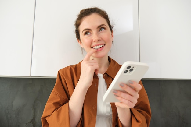 Portrait of excited young woman smiling and looking with thinking face while using shopping app