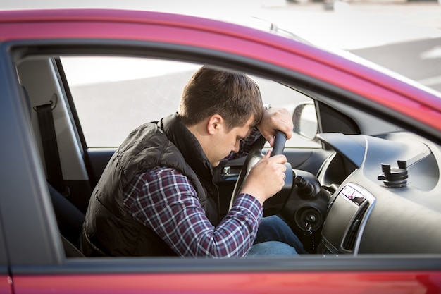 Portrait of exhausted young man sleeping on drivers seat while driving a car