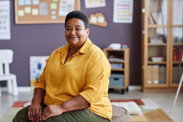 Portrait of experienced african american female teacher or coach in yellow shirt sitting in front of