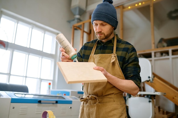 Portrait of experienced young man carpentry worker applying glue adhesive material on wooden board