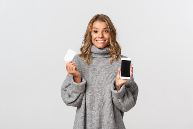 Портрет выразительной молодой женщины с мобильным телефоном и кредитной картой