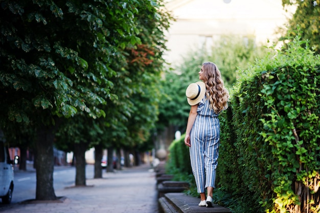 Portrait of a fabulous young woman in striped overall walking on the barrier in the park.