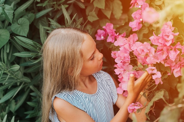 Volto ritratto di candida bambina di otto anni su sfondo di piante verdi e ammirato godersi l'odore dei fiori rosa durante una vacanza estiva viaggio gen z concetto di salute mentale bagliore