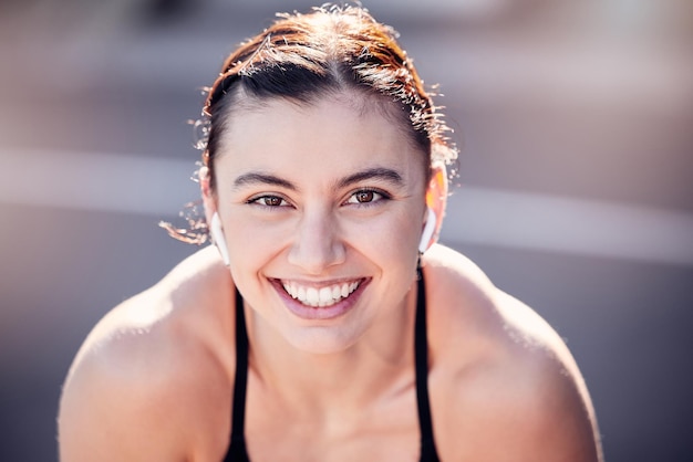 Portrait face and fitness with a sports woman listening to music while running outdoor for cardio exercise Happy smile and workout with a female runner training alone for an endurance marathon