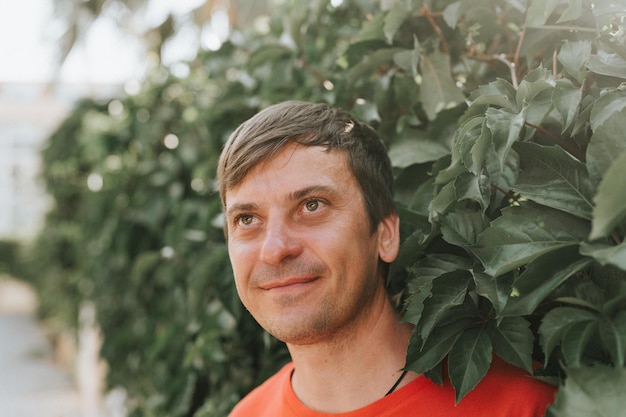 Portrait of face happy smiling unshaven mature 40 years man solo traveler with stubble and brown eyes on the background of green trees plants in nature on sunny summer day on vacation travel getaway