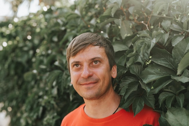 Portrait of face happy smiling unshaven mature 40 years man solo traveler with stubble and brown eyes on the background of green trees plants in nature on sunny summer day on vacation travel getaway