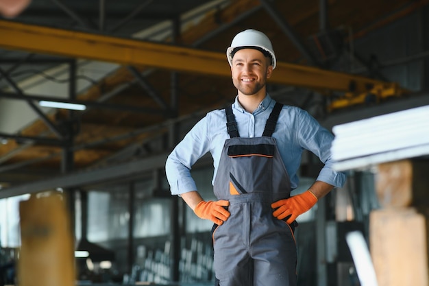 Portrait of factory worker in protective uniform and hardhat standing by industrial machine at production line People working in industry