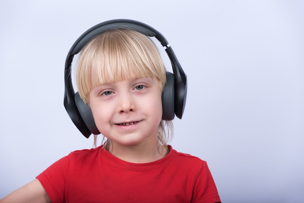 Portrait of fair-haired boy in headphones on white background closeup.