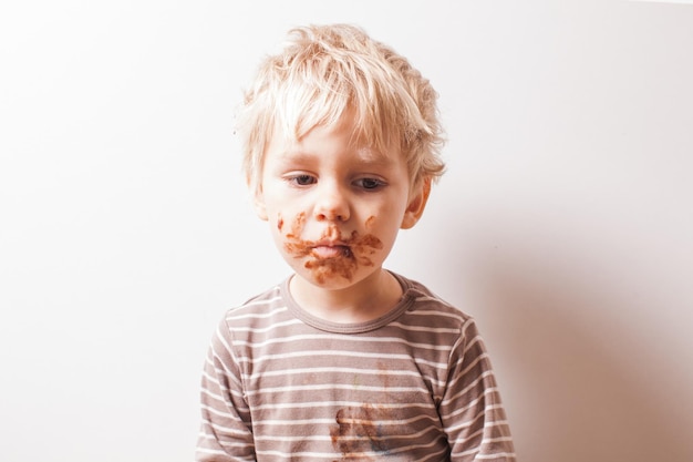 Portrait of fair-haired boy with chocolate on his face isolated on white