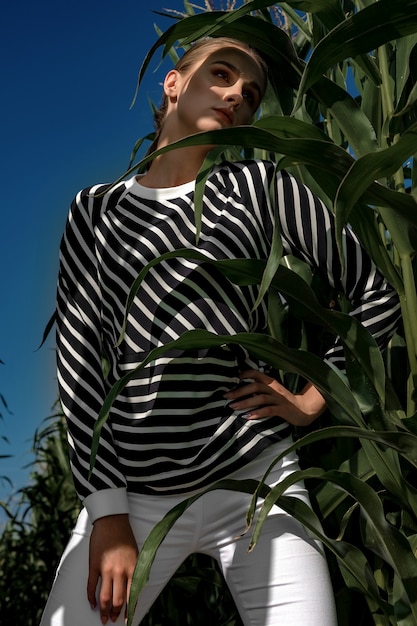 Портрет белокурой девушки в модной и стильной одежде, среди листвы кукурузного поля.