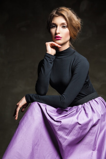 Portrait of fair-haired model with pink lips sitting in studio and looking away.