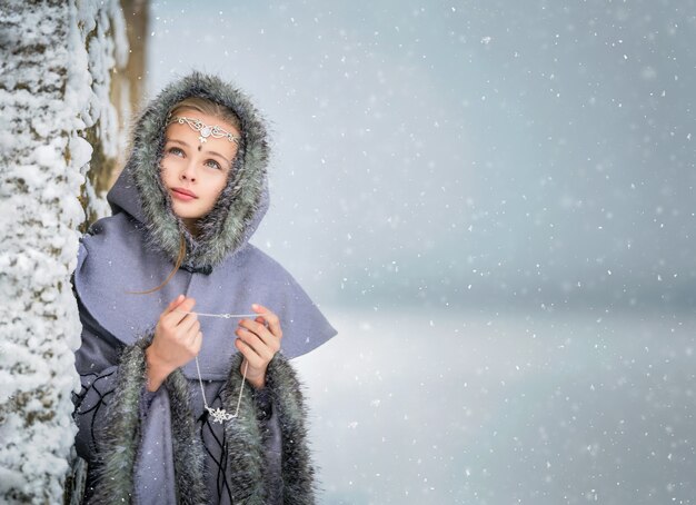 Портрет сказочной девушки-эльфийки с украшением в руках на фоне старинной крепости зимой