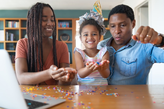 Ritratto di una famiglia che festeggia il compleanno in linea su una videochiamata con il laptop mentre si è a casa.