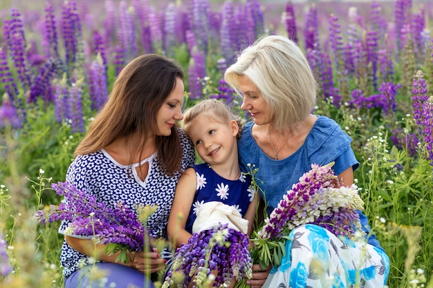 Portrait  of family generation: Happy grandmother, daughter and granddaughter on a flowering lupine field. Mother's day concept