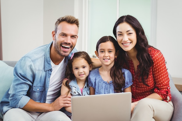 Portrait of family smiling and using laptop on sofa