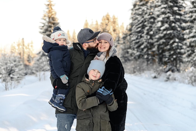 雪の中で立っている家族の肖像画。父親は小さな子供を腕に抱き、妻と息子は雪の中で幸せな家族の概念を彼の隣に立っています。