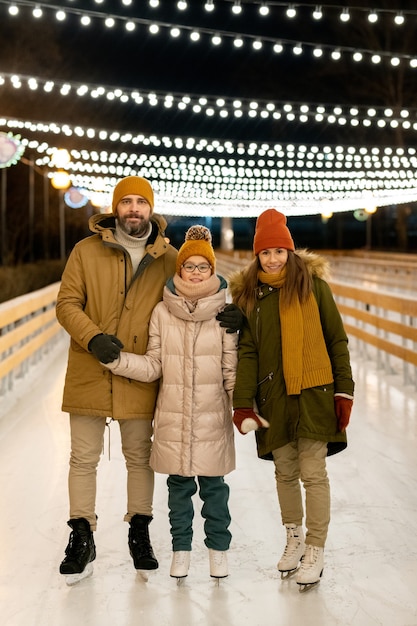 Ritratto di una famiglia di tre persone che sorride alla telecamera mentre pattina sulla pista di pattinaggio nel parco