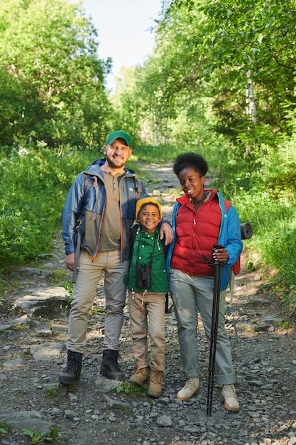 Photo portrait of family with their son smiling at camera while go hiking in the forest