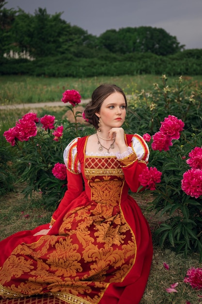 Photo portrait of fantasy medieval girl princess in vintage red dress woman sitting in peony