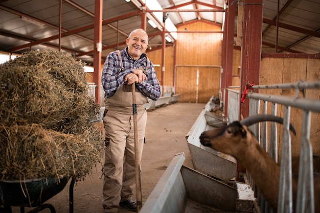 Photo portrait of farmer standing by wheelbarrow with hay food and working in the farmhouse