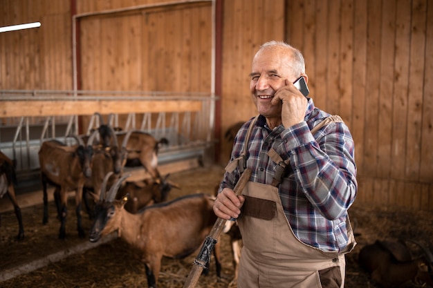 Ritratto di contadino parlando al cellulare e in piedi in casa colonica