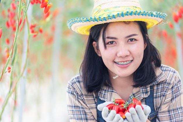 Portrait of farmer young woman in uniform smiling holding fresh red tomatoes on hands after freshly harvest tomato organic food garden small business concept