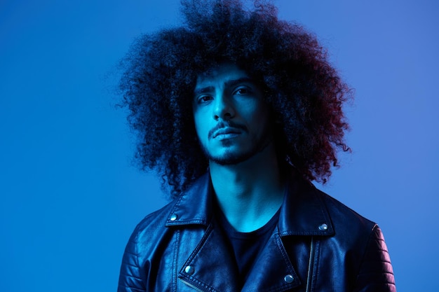 Portrait of fashion man with curly hair on blue background multinational colored light black leather jacket trend modern concept