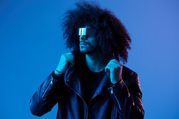 Portrait of fashion man with curly hair with stylish glasses on blue background multinational colored light black leather jacket trend modern concept