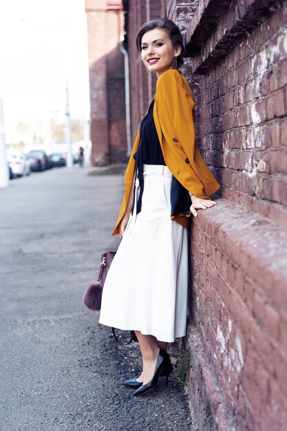 Portrait fashion woman walking on street . She wears yellow jacket, smiling to side.