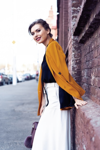 Portrait fashion woman walking on street . She wears yellow jacket, smiling to side.