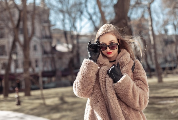 Portrait of fashion woman in warm fur coat gloves and sunglasses in city