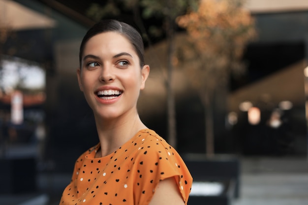 Portrait fashion woman in yellow dress walking on street of the city, smiling to side.