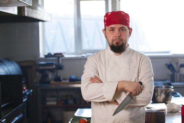 Portrait of a fashionable chef in bandana holding a knife in a kitchen, concept of cooking and Haute cuisine