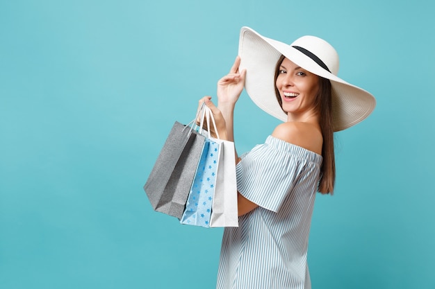 Portrait fashionable elegant fashion beautiful caucasian woman in summer dress, white large wide brim sun hat holding packages bags with purchases after shopping isolated on blue pastel background.