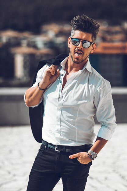 Photo portrait of fashionable man sticking out tongue while standing on building terrace