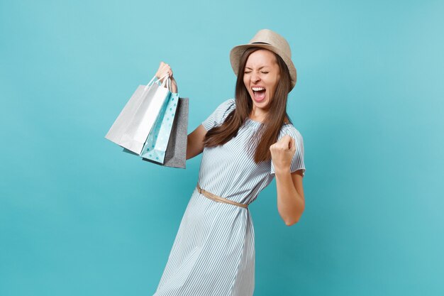 Portrait fashionable smiling beautiful caucasian woman in summer dress, straw hat holding packages bags with purchases after shopping isolated on blue pastel background. Copy space for advertisement.
