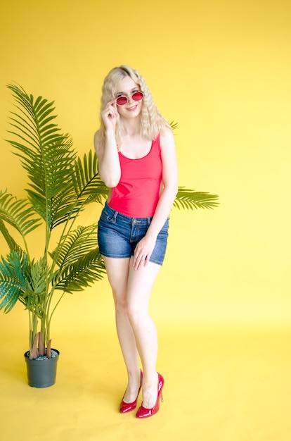 Foto il ritratto della donna alla moda indossa la camicia rossa e gli shorts dei jeans concetto di vacanza di viaggio occhiali da sole rossi delle scarpe