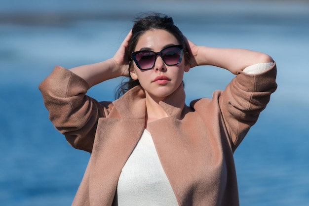 Portrait of fashionable young woman with long hair red plump lips and sunglasses dressed in beige co