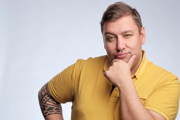 Portrait of a fat caucasian man in yellow tshirt posing in studio on gray background