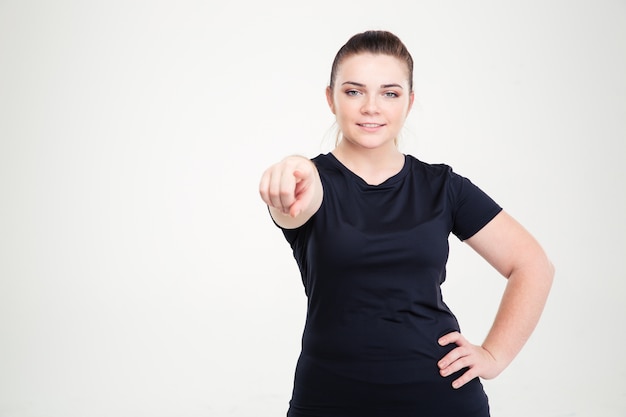 Ritratto di una donna grassa in abbigliamento sportivo che punta il dito isolato su un muro bianco