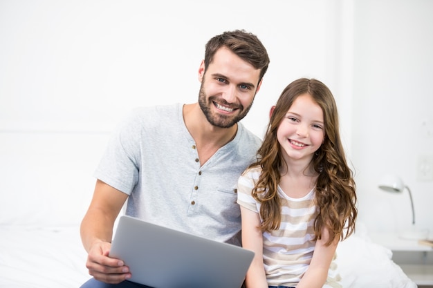 Portrait of father and daughter using laptop on bed