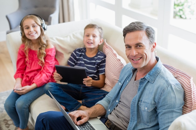 Portrait of father and kids using laptop and digital tablet in living room