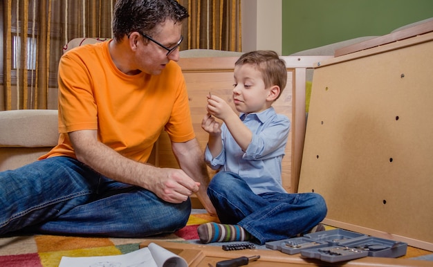 Portrait of father and son assembling with tools a new furniture for home. Family leisure concept