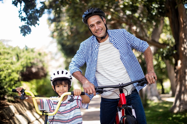 Portrait of father and son standing with bicycle in park