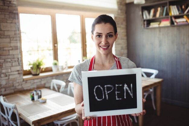 Portrait of female baker holding open signboard