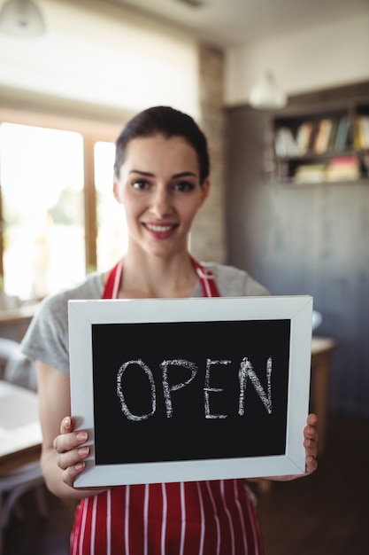 Portrait of female baker holding open signboard