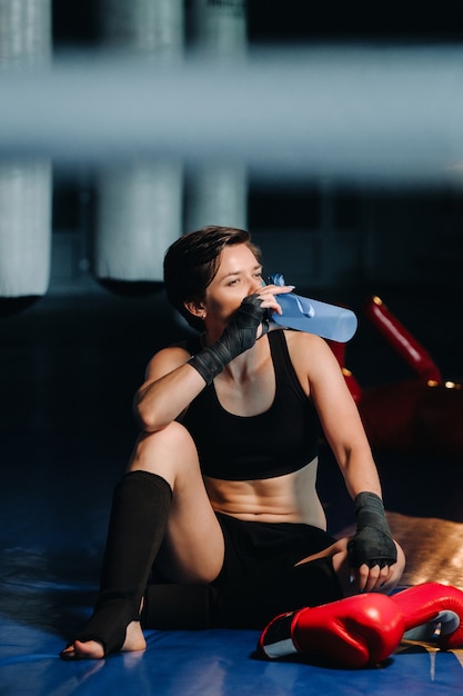 Portrait of a female boxer in red gloves in the gym after a workout with a bottle of water.