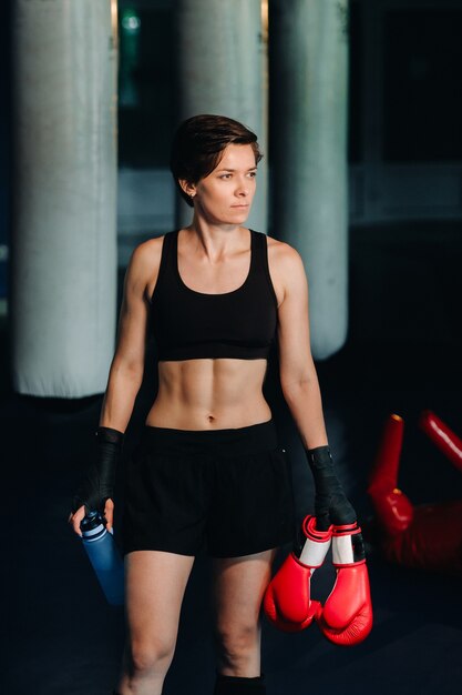 Portrait of a female boxer in red gloves in the gym after a workout with a bottle of water