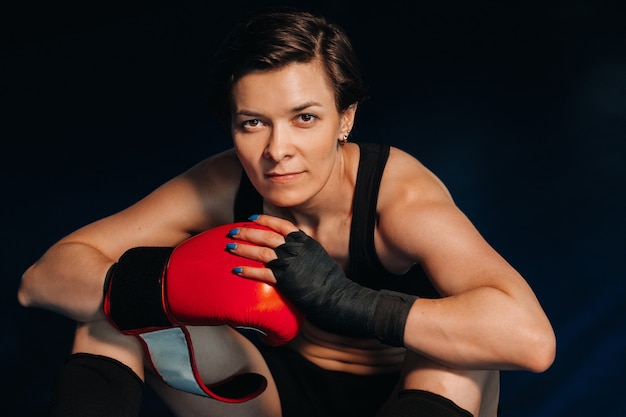 Портрет женщины-боксера в красных перчатках в тренажерном зале во время тренировки.